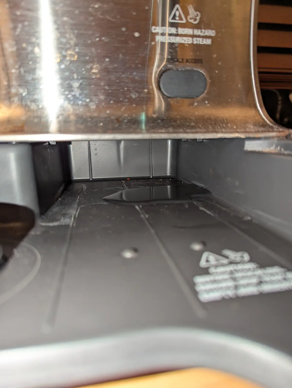A close-up photo shows the inside of a coffee machine's steam wand area, covered in water droplets and grime, with a warning…