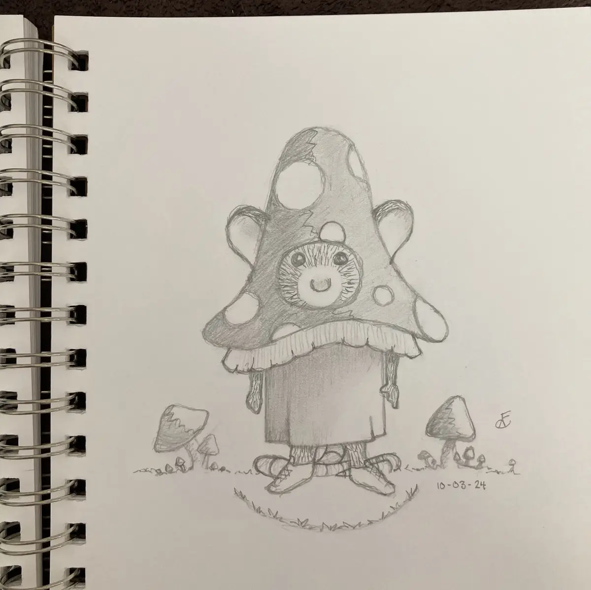 A pencil sketch in a spiral-bound notebook shows a whimsical, anthropomorphic mushroom creature with a large, spotted cap…