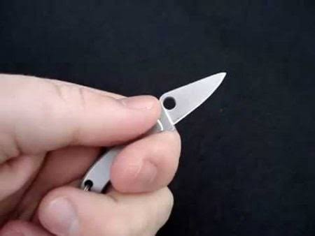 A close-up image shows a person's hand holding a small, silver pocket knife with the blade partially extended against a dark…