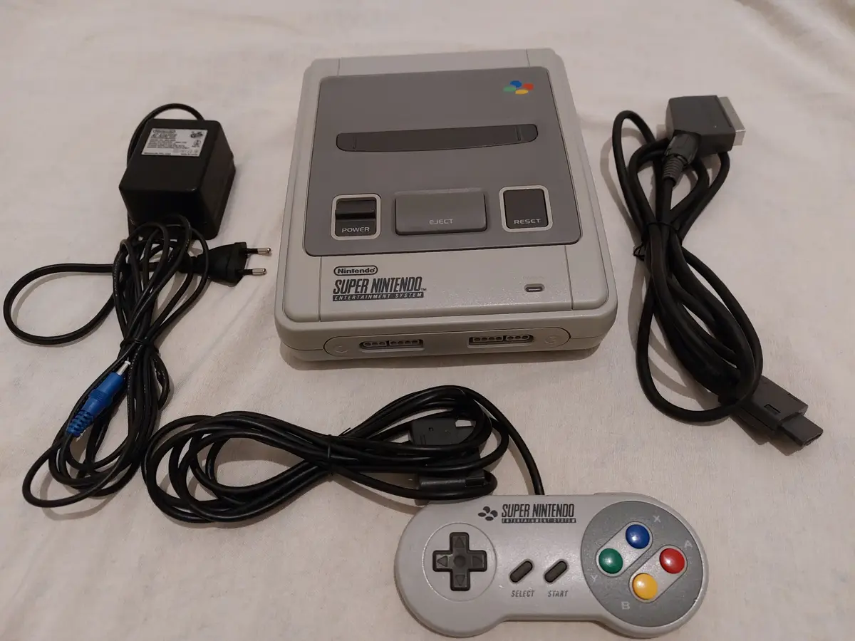 A complete Super Nintendo Entertainment System (SNES) console is laid out on a white fabric surface, including the gray…