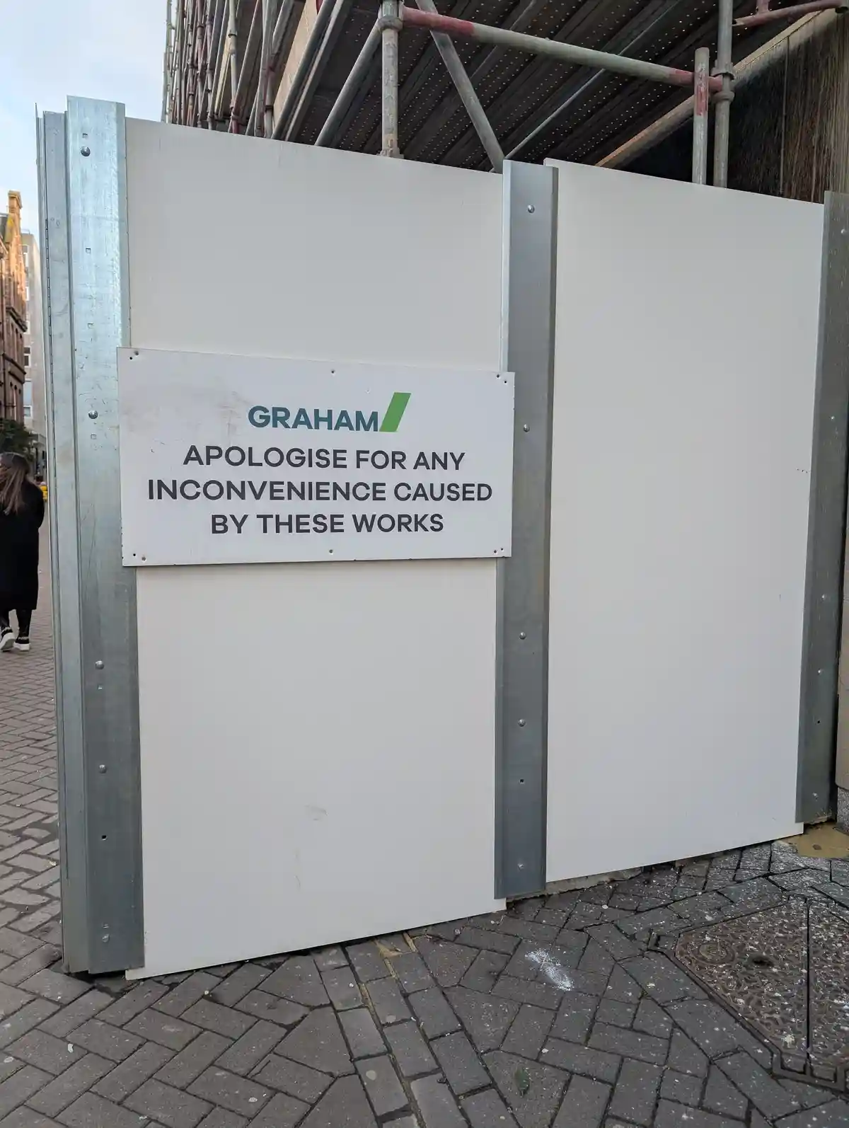A white construction hoarding with a sign from 'GRAHAM' that reads 'APOLOGISE FOR ANY INCONVENIENCE CAUSED BY THESE WORKS'…