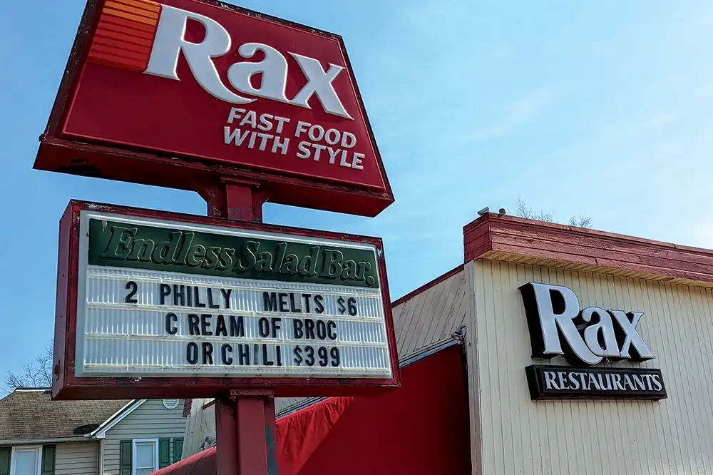 An outdoor photo of a Rax fast food restaurant sign with a marquee board below it. The marquee reads 'Endless Salad Bar' and…