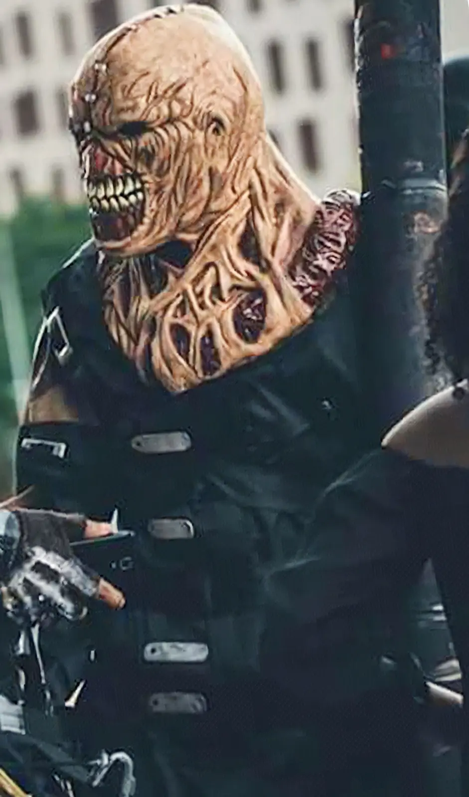 A person wearing a grotesque, textured, flesh-like monster mask with exposed teeth and multiple eye sockets, dressed in a…