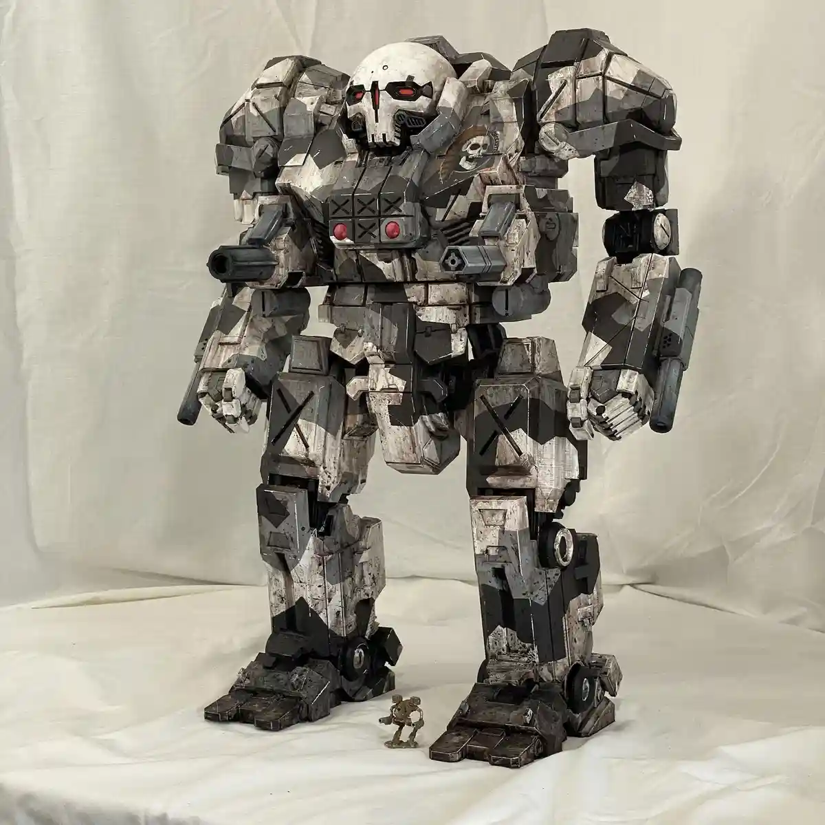 A large, heavily weathered and camouflaged humanoid robot with a skull-like face, red glowing eyes, and multiple weapons…