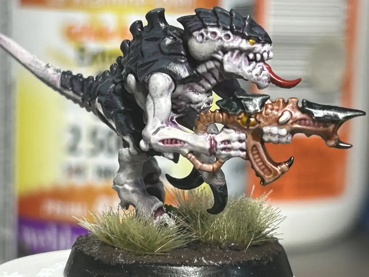 A painted miniature of a monstrous, reptilian creature with black spines, white flesh, and a red tongue, holding a bone-like…