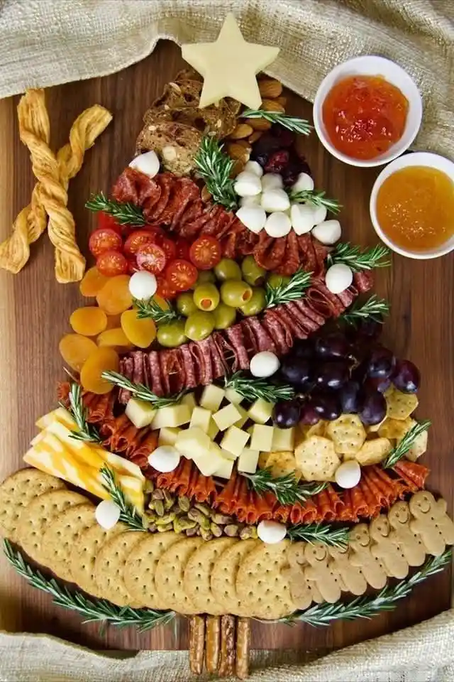 a festive charcuterie board arranged in the shape of a christmas tree on a wooden cutting board, featuring layers of cheese…