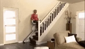 A woman in a red shirt and dark pants is shown in six sequential frames riding a white stair lift up a staircase inside a…