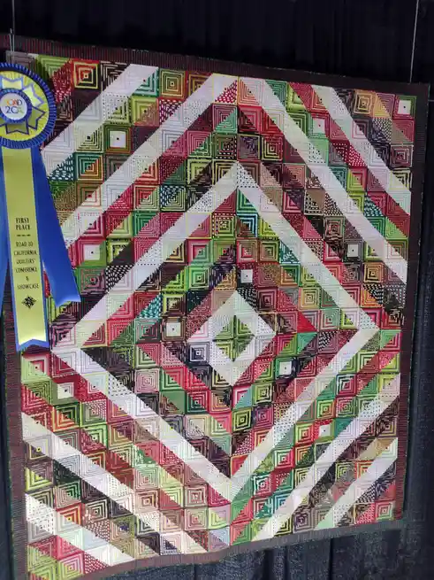 A colorful, geometric quilt with a repeating pattern of concentric squares in red, green, white, and black, displayed on a…