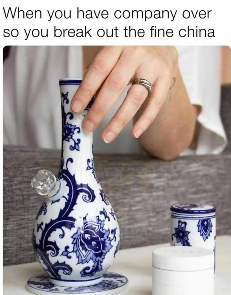 A hand with a ring gently touches a blue and white porcelain bong, which is styled like fine china with floral patterns…