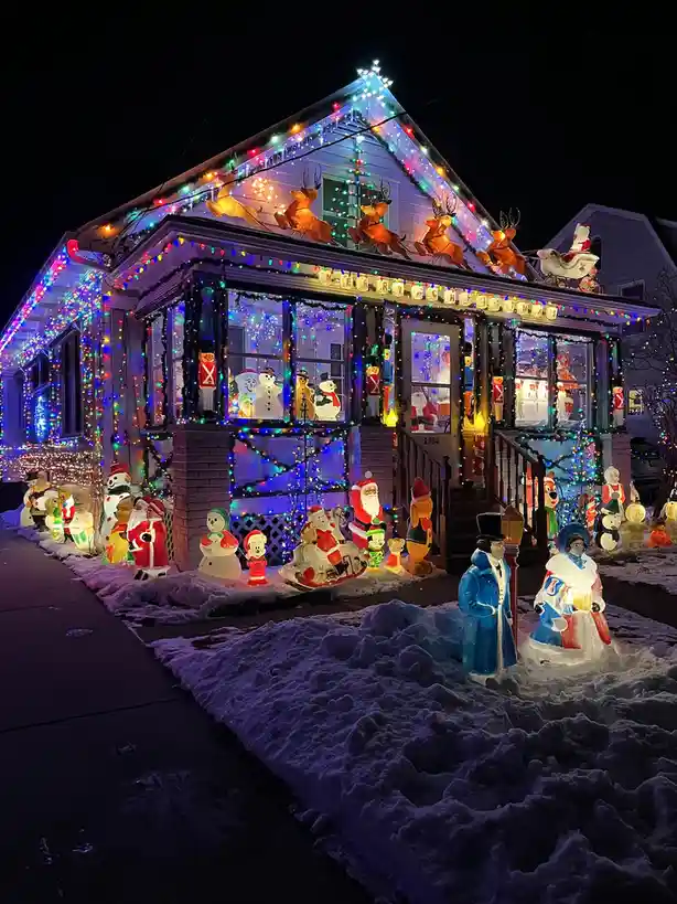 A house is extravagantly decorated for Christmas at night with colorful string lights, inflatable reindeer on the roof, and…