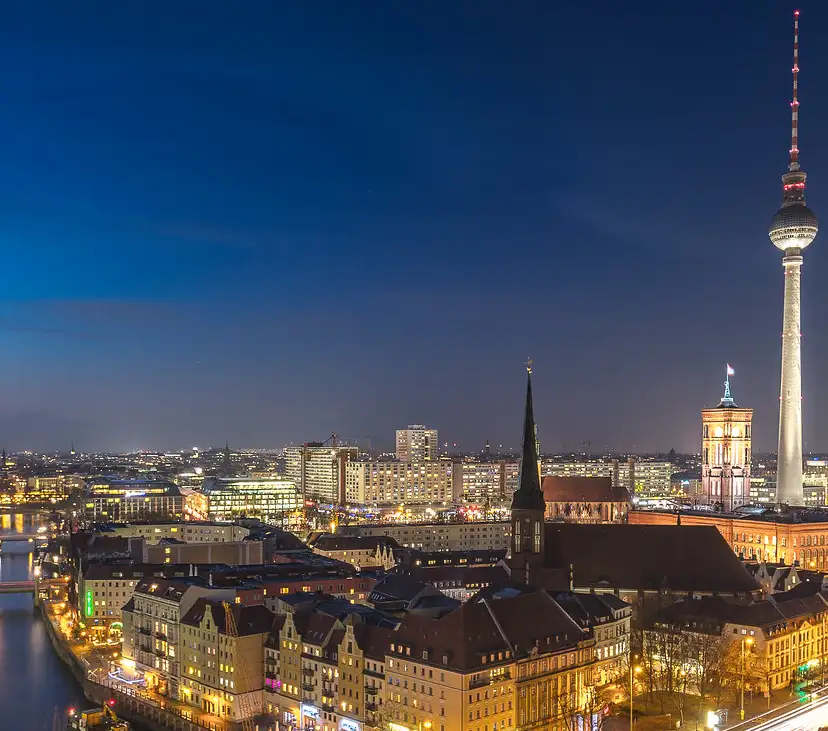 A nighttime cityscape of Berlin, Germany, featuring the iconic Fernsehturm television tower on the right, illuminated…