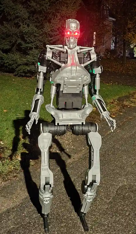 A full-body Terminator-style robot with glowing red eyes stands on a paved path at night, casting a long shadow on grass and…