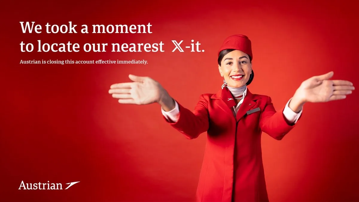 A smiling Austrian Airlines flight attendant in a red uniform and hat stands against a solid red background with arms…