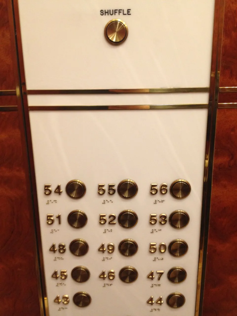 An elevator panel with gold buttons for floors 44 through 56, arranged in a grid, and a single 'SHUFFLE' button at the top…