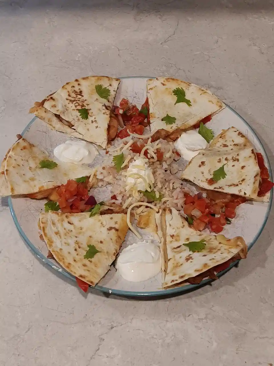 A plate of food arranged in a circle, featuring triangular tortilla wedges surrounding a central pile of rice, shredded…