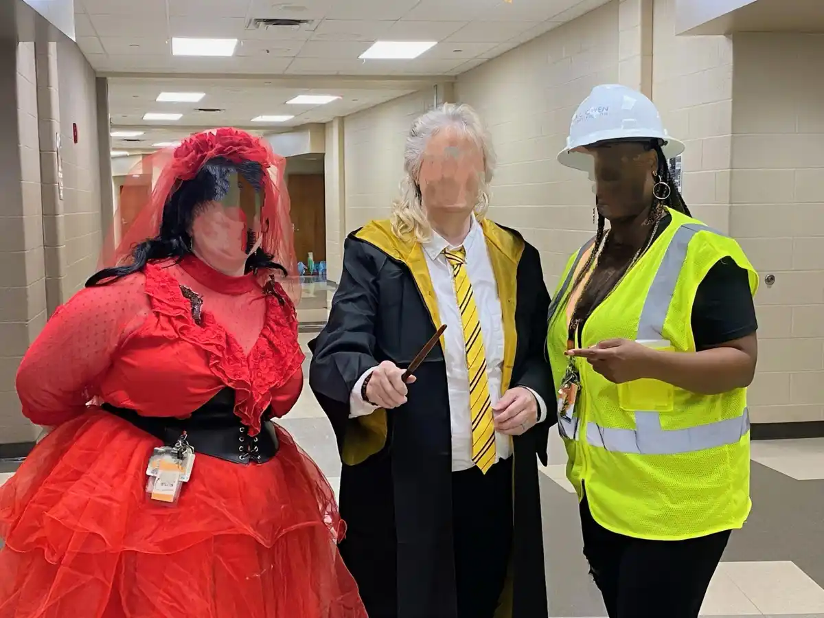 Three people stand in a hallway, their faces blurred. The person on the left wears a red Victorian-style dress with a veil…