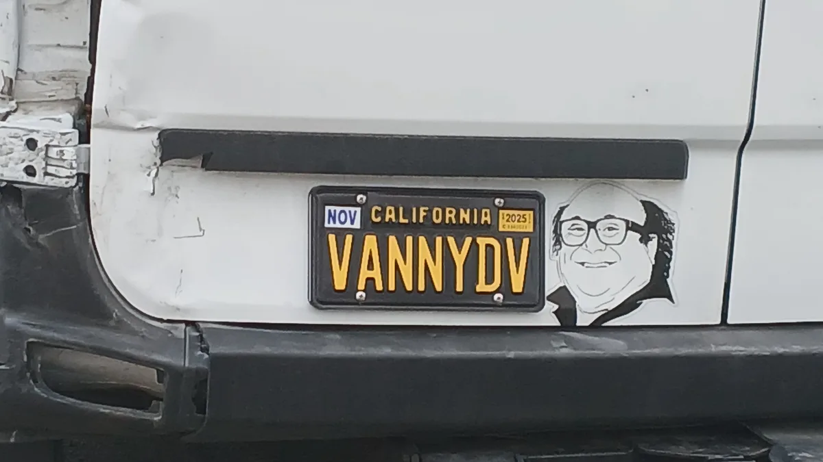 A close-up of a California license plate on a white vehicle, displaying the registration 'VANNYDV' in yellow letters on a…