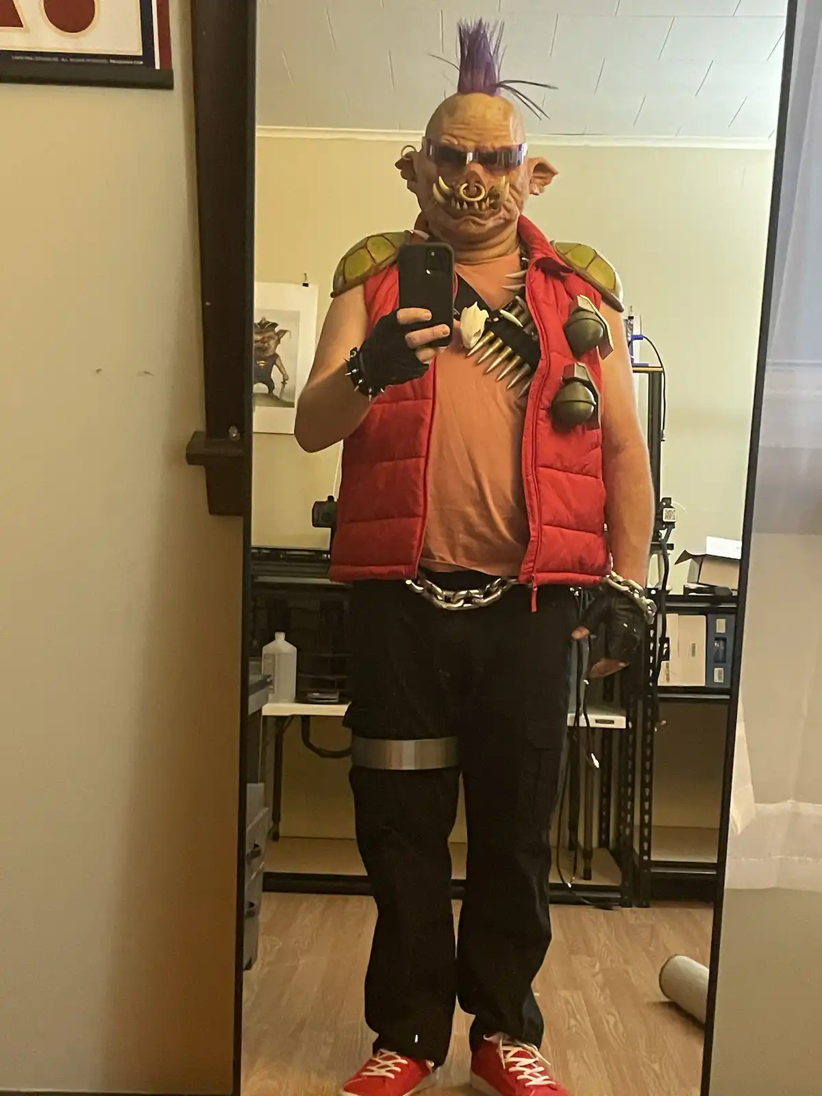A person in a full-body costume resembling a turtle mutant with a purple mohawk, sunglasses, and a red puffer vest over an…
