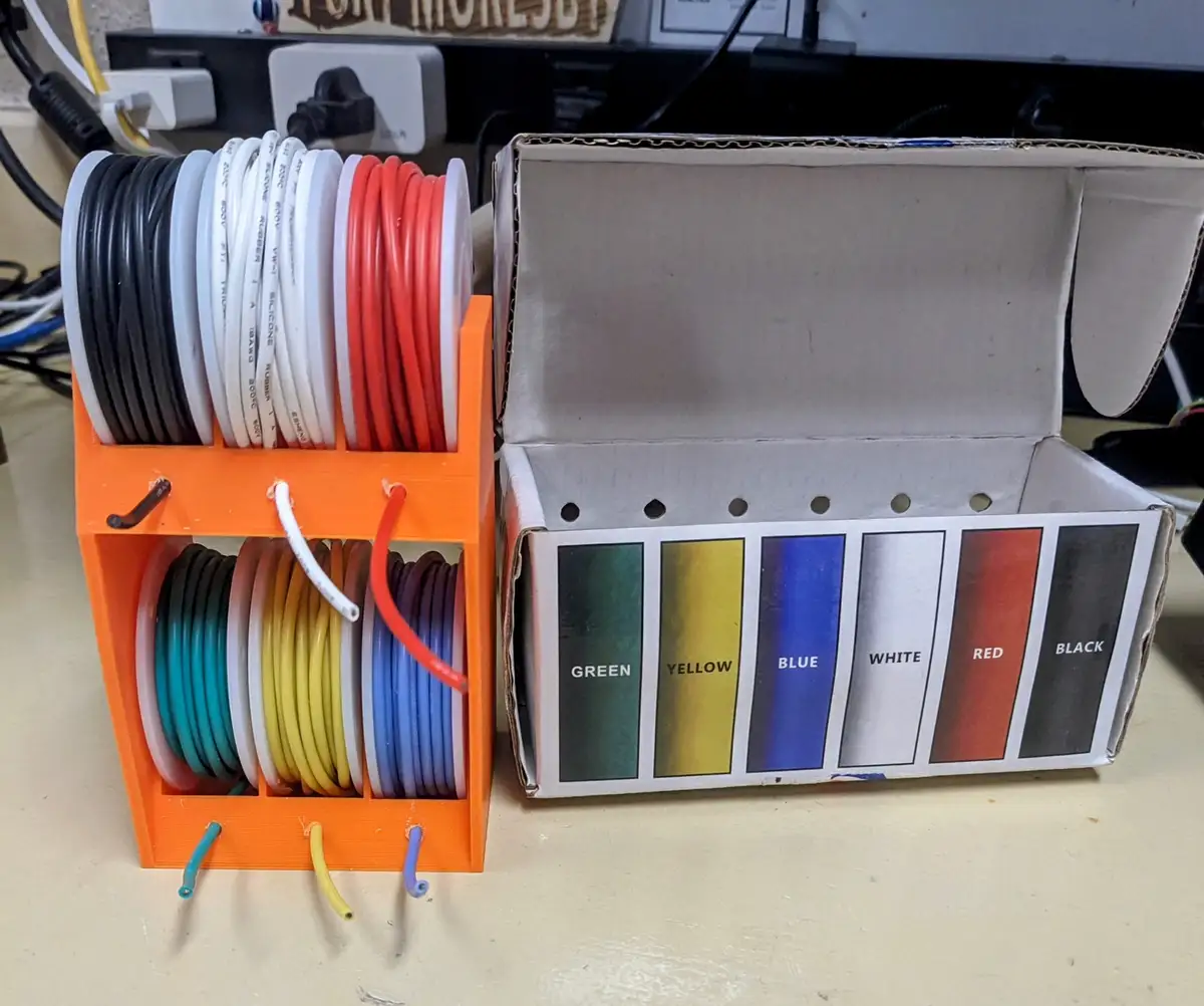 An orange 3D-printed cable organizer holds neatly spooled wires in various colors, next to a cardboard box with color…