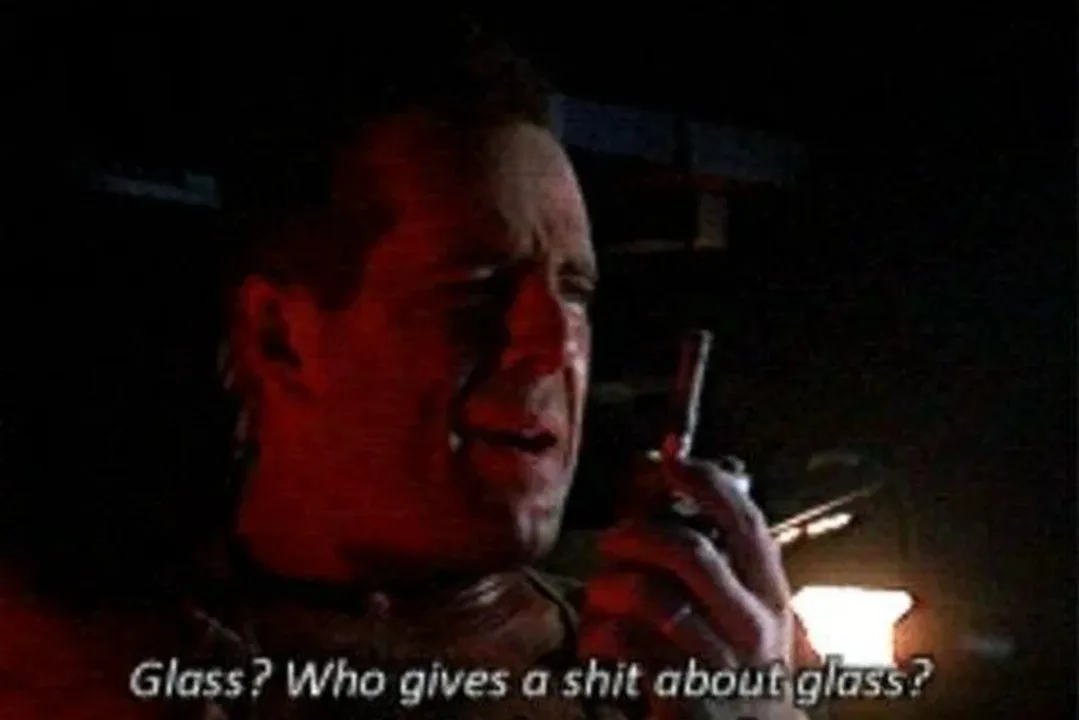 A man in a dark, red-lit environment holds a walkie-talkie to his mouth and speaks with a dismissive expression. The…