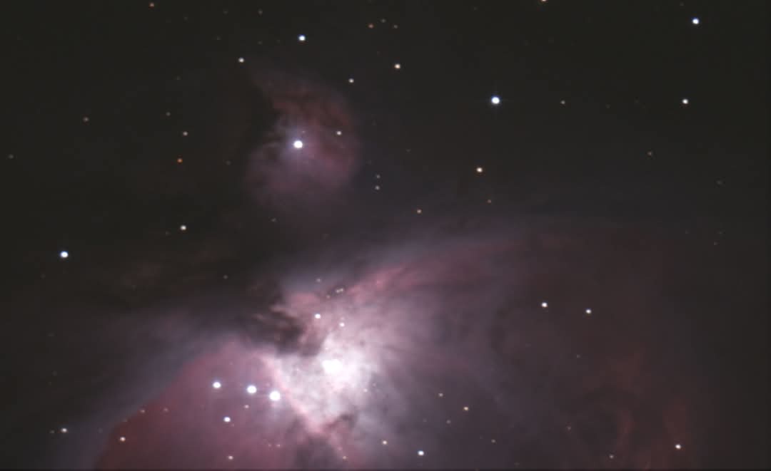 A deep-space photograph shows a dark cosmic background filled with numerous stars and a prominent pinkish-purple nebula with…