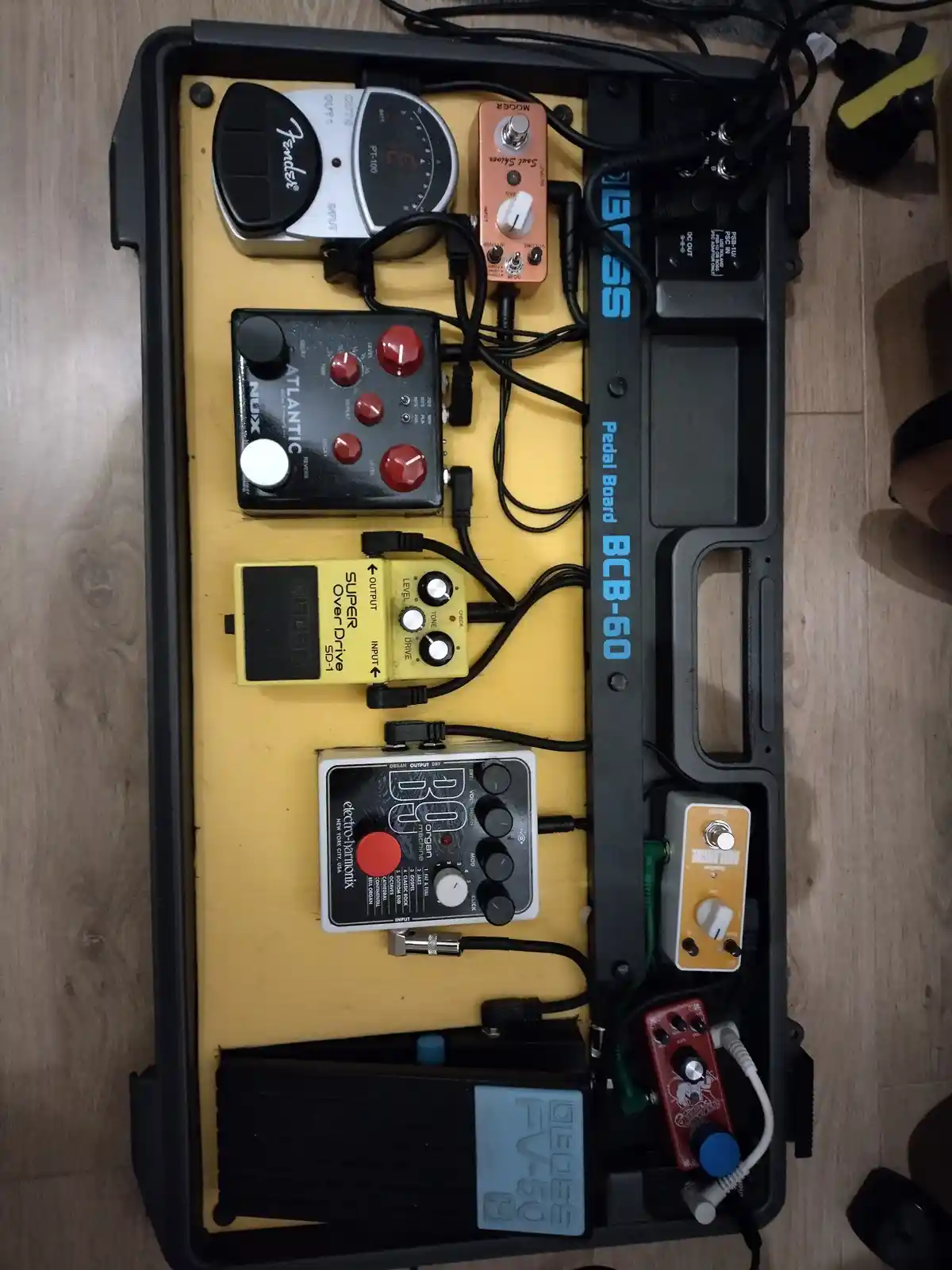 An overhead shot of a black Boss BCB-60 pedalboard filled with various guitar effects pedals, including a Fender PT-100, a…