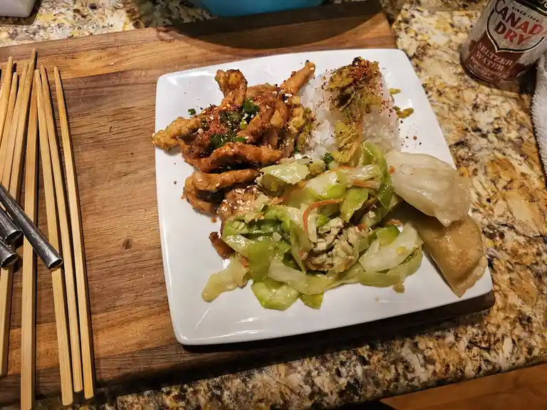 A white plate of home-cooked Asian-style food, including stir-fried chicken, rice, cabbage stir-fry, and dumplings, sits on…