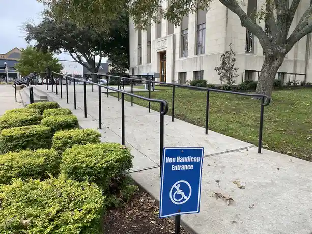 A blue sign with a white wheelchair symbol crossed out and the text 'Non Handicap Entrance' is placed at the base of a…