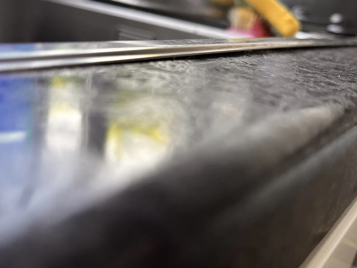A close-up, blurry photo shows a shiny metal object, likely a knife or tool, resting on a dark, textured surface. The…