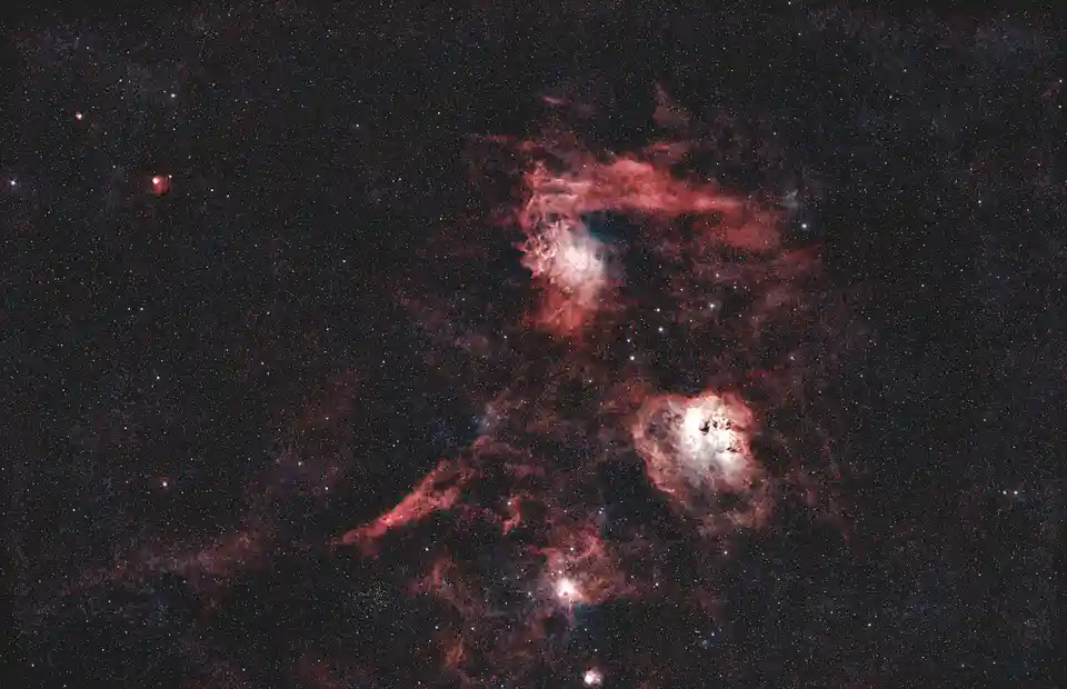 A deep-space photograph shows a dark cosmic background filled with countless stars and glowing red and white nebulae…