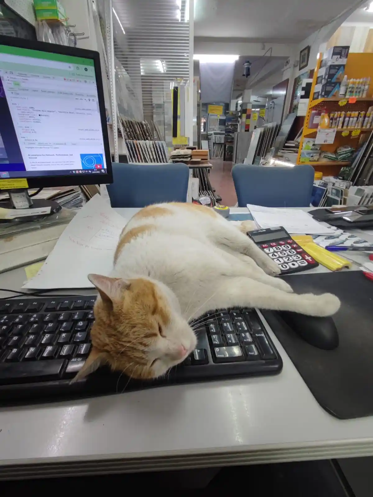 A ginger and white cat is sleeping soundly on a computer keyboard, its body stretched out across the keys and mousepad, with…