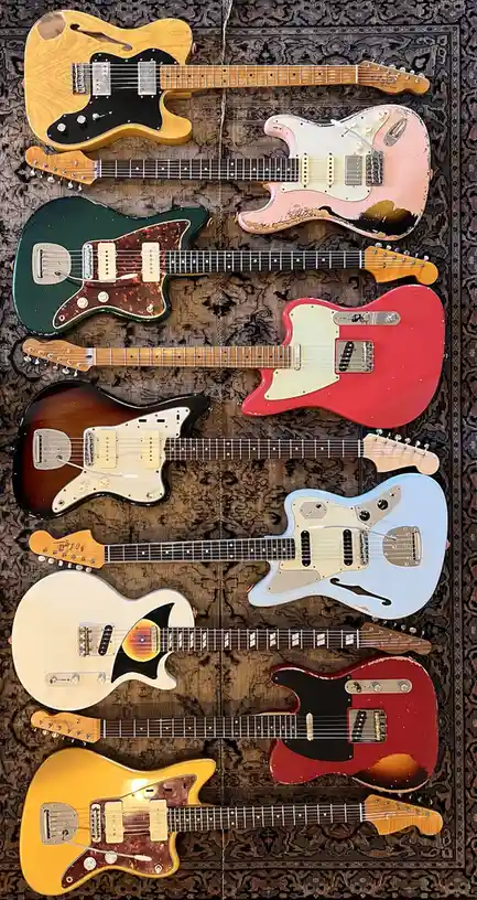 An overhead photo shows ten electric guitars of various colors and models arranged in two columns on a patterned rug. The…