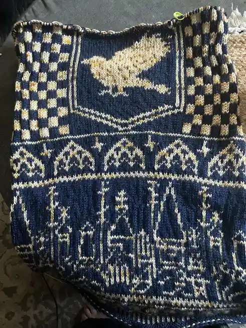 A close-up photo of a hand-knitted textile, likely a blanket or scarf, featuring intricate patterns in navy blue, cream, and…