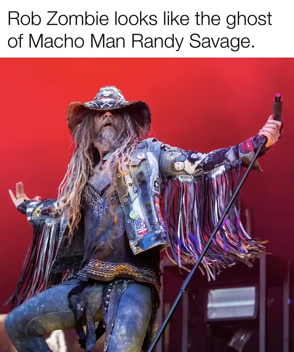 A photo of Rob Zombie performing on stage, wearing a wide-brimmed hat, a heavily patched and fringed denim jacket, and…