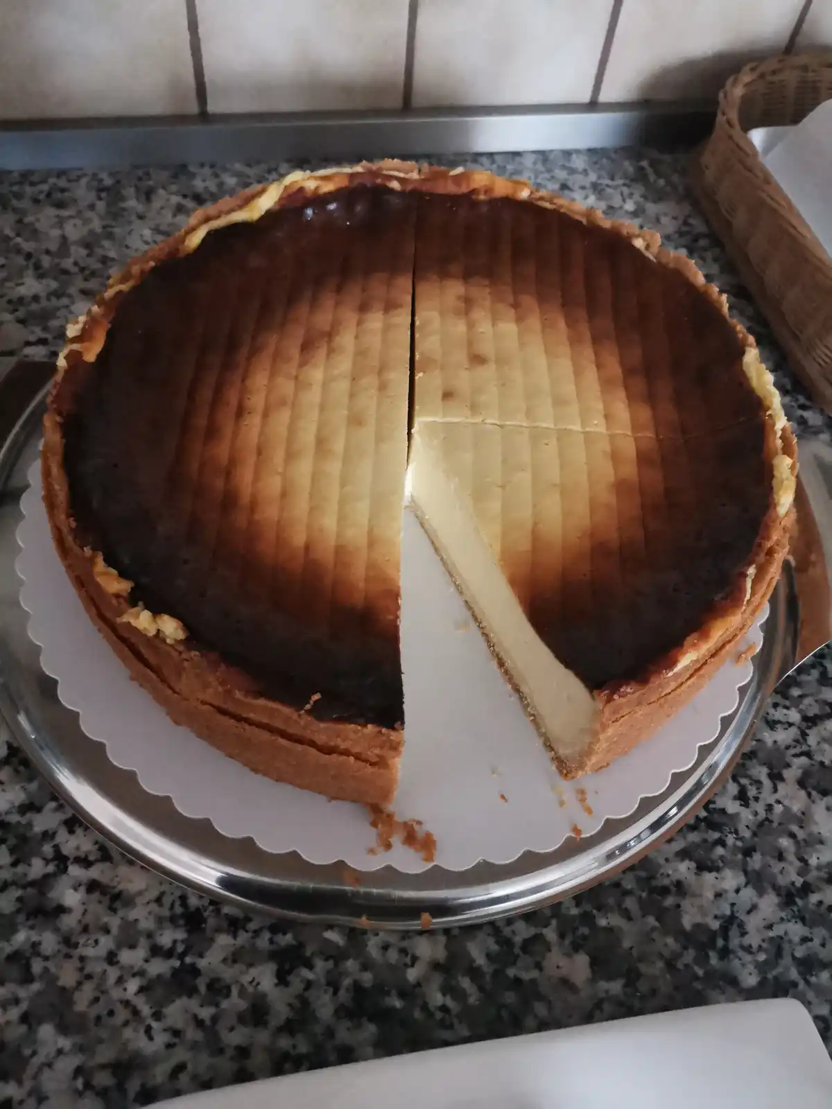 A round cheesecake with a golden-brown, striped top sits on a silver platter, one slice cut out. The text overlaid reads 'i…