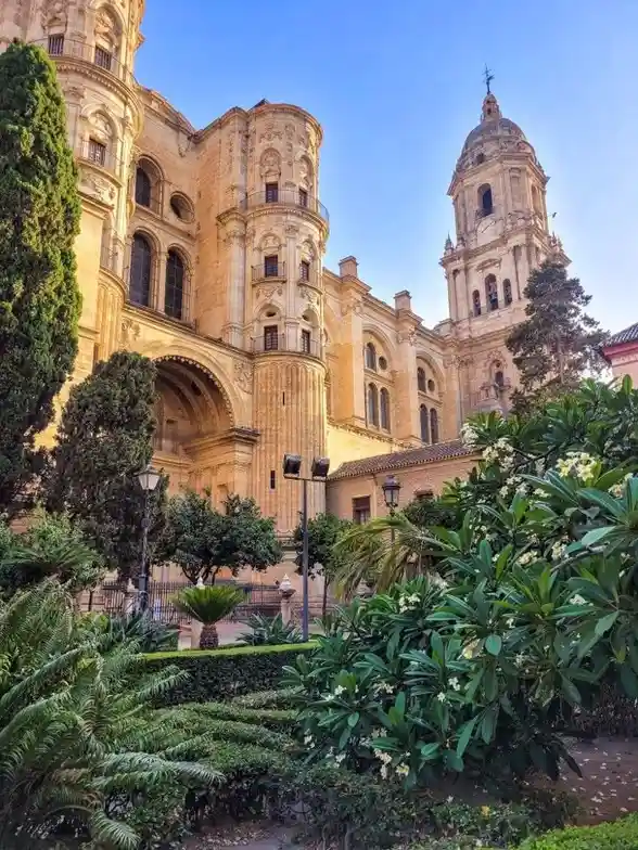 a photograph of a grand, ornate stone cathedral with multiple towers and arched windows, set against a clear blue sky. Lush…