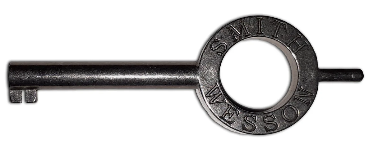 A close-up of a metallic, vintage-style key with a circular bow that has the words 'SMITH & WESSON' engraved around its…