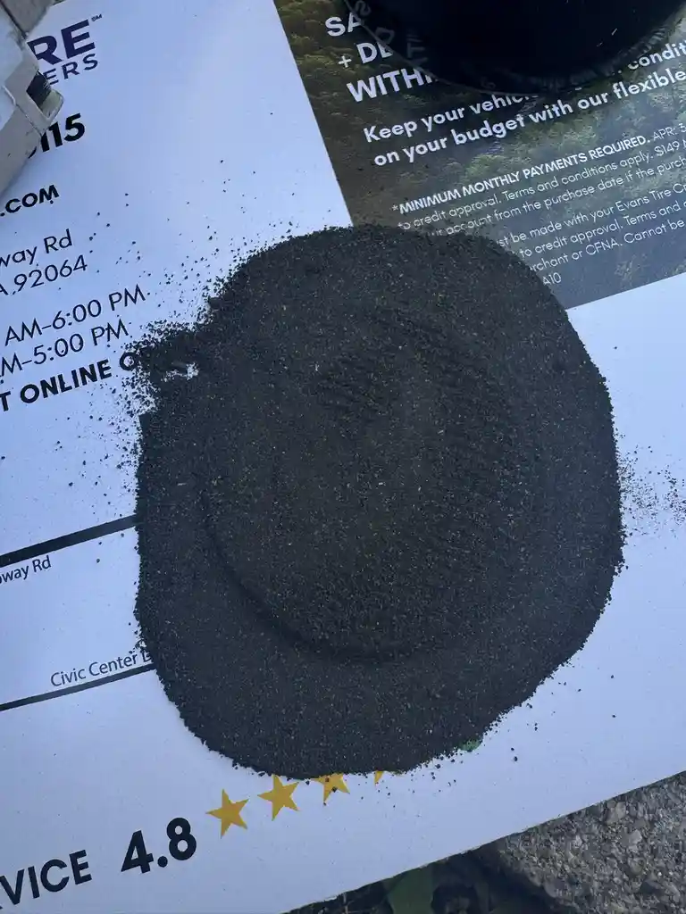A pile of black sand or grit sits on top of a business flyer that advertises tire services and shows a 4.8-star rating. The…