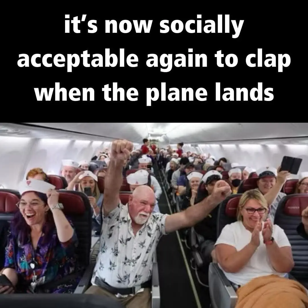 An airplane cabin filled with passengers, many wearing white hats, enthusiastically clapping and cheering as the plane…