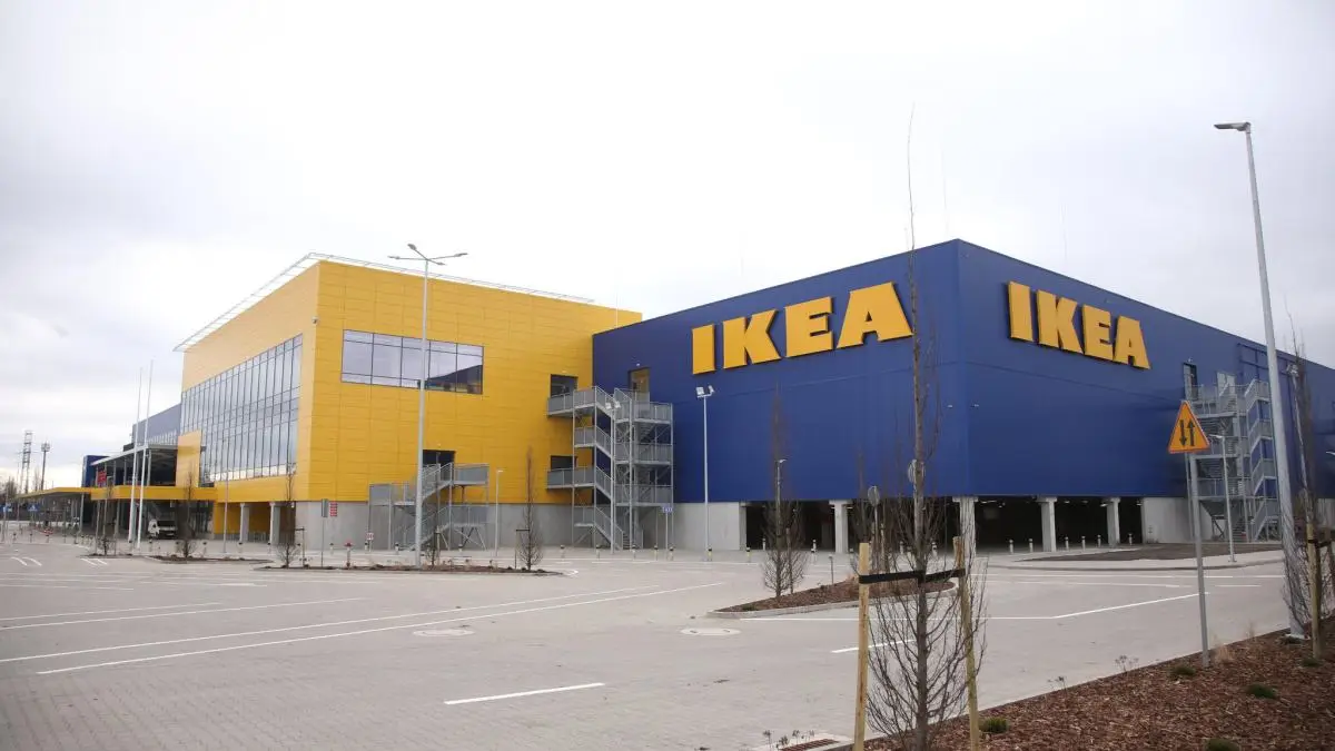An exterior shot of an IKEA store with its iconic blue and yellow facade, large 'IKEA' lettering, and empty parking lot…