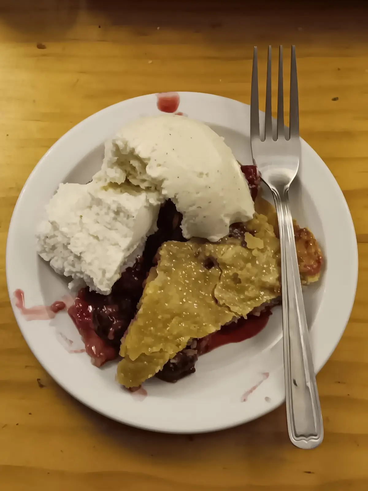 A close-up photo shows a partially eaten slice of fruit cobbler on a white plate, topped with a scoop of vanilla ice cream…