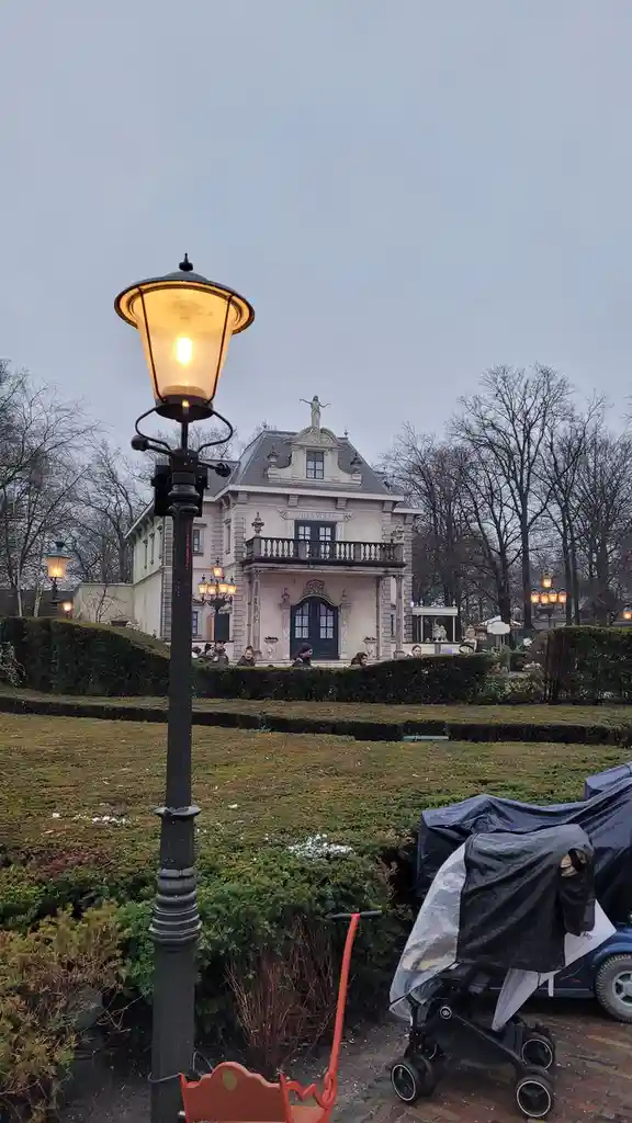 A photo of a grand, ornate villa labeled 'VILLA VOLTA' under an overcast sky, with a lit vintage streetlamp in the…