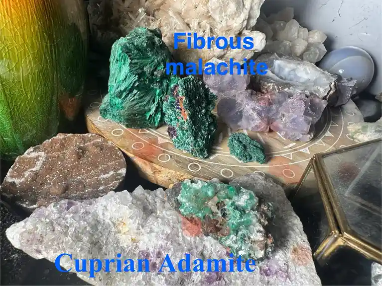 A collection of various colorful minerals and crystals displayed on a wooden board and dark surface, with blue text labels…