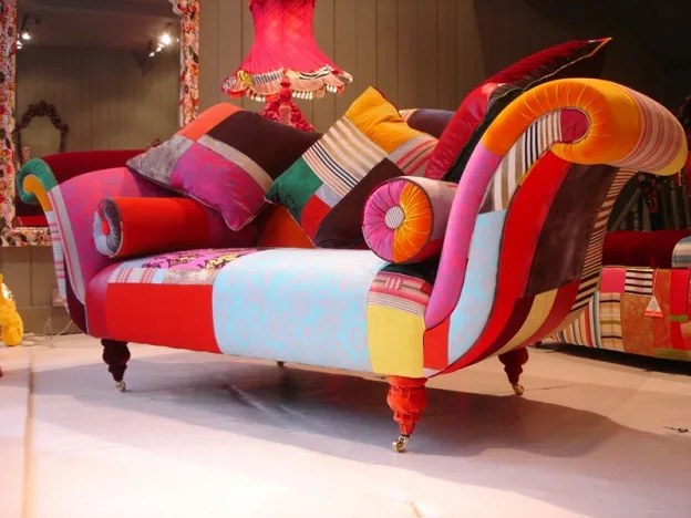 a visually striking, ornate chaise lounge upholstered in a chaotic patchwork of colorful fabrics including stripes, solids…