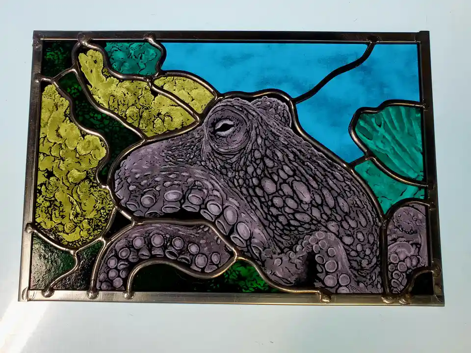 A stained glass artwork depicts a purple octopus with detailed suckers, set against a background of blue, green, and gold…
