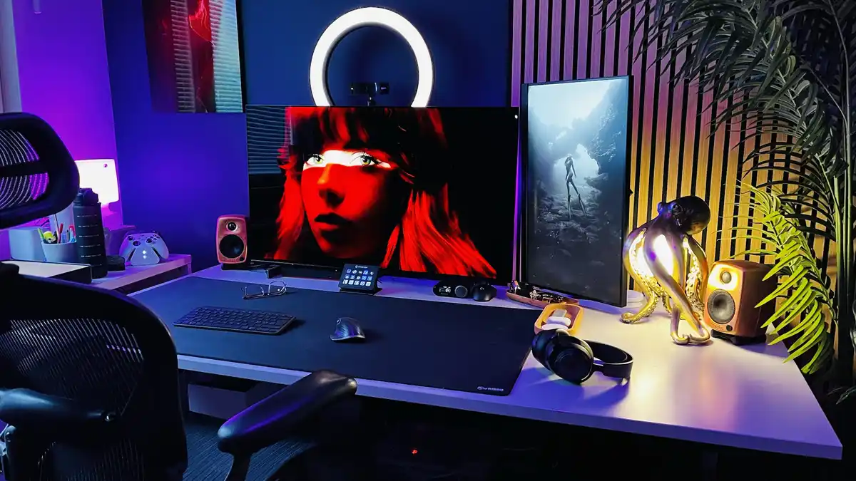 A well-lit, modern gaming or streaming setup with dual monitors, a ring light, and various peripherals. The left monitor…