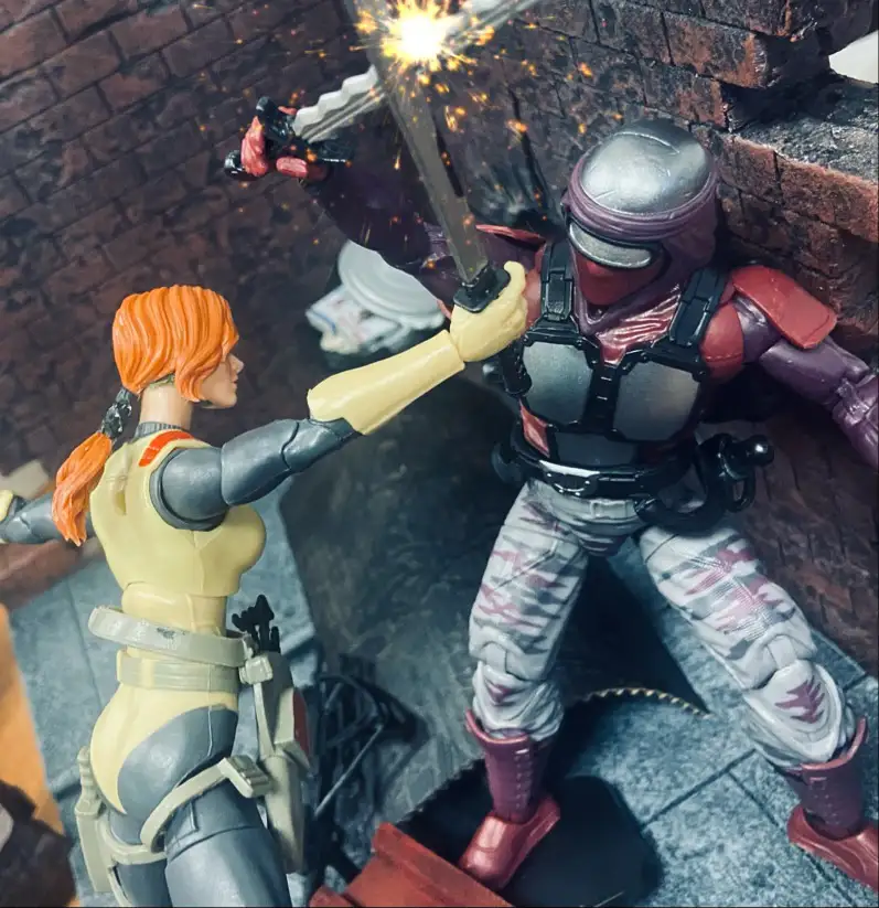 Two action figures are locked in combat, one with orange hair and a yellow outfit, the other in a red and grey armored suit…