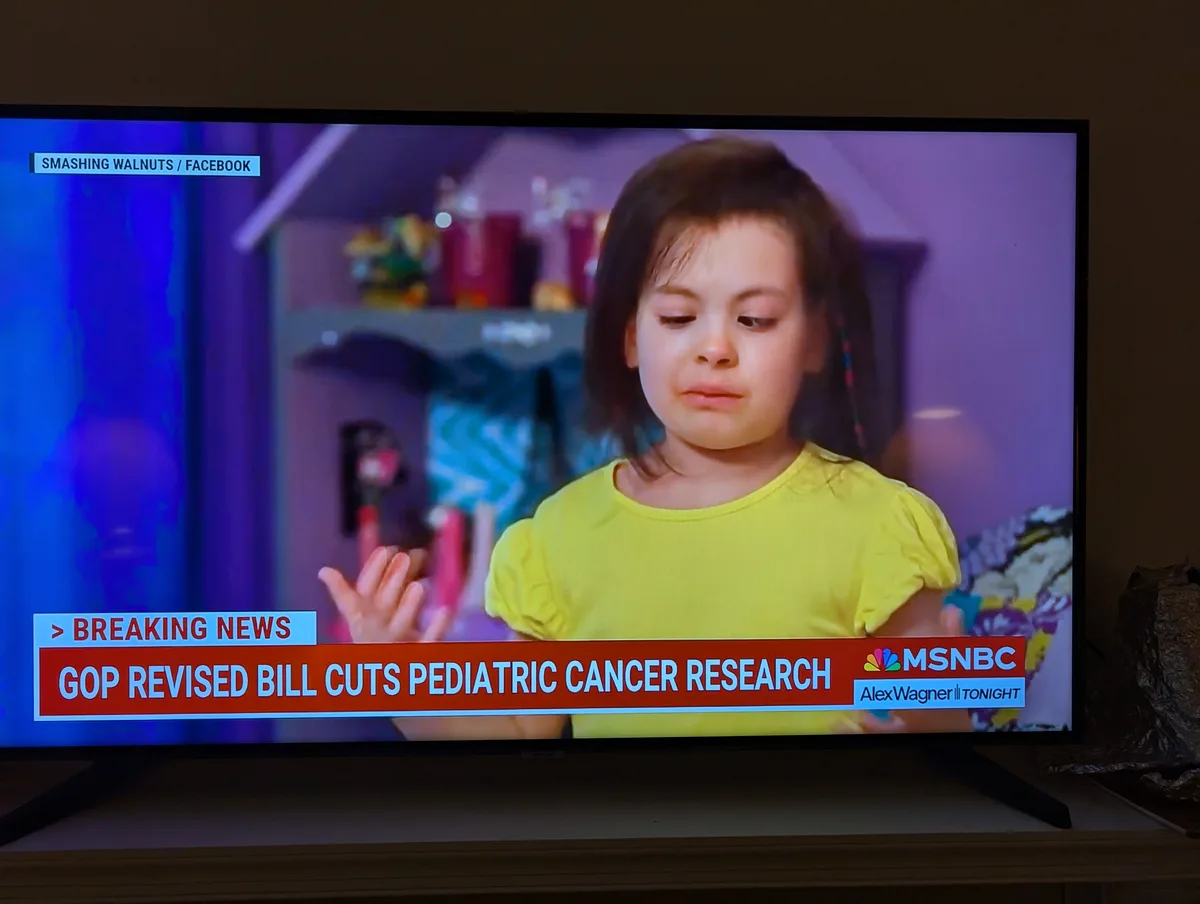 A television screen displays a news broadcast with a young girl in a yellow shirt looking sad and disappointed. The news…