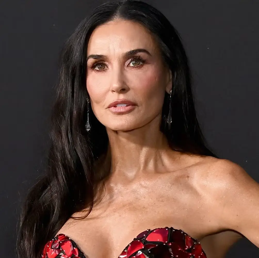 A woman with long dark hair and a red bejeweled strapless top stares directly at the camera with a serious, unimpressed…