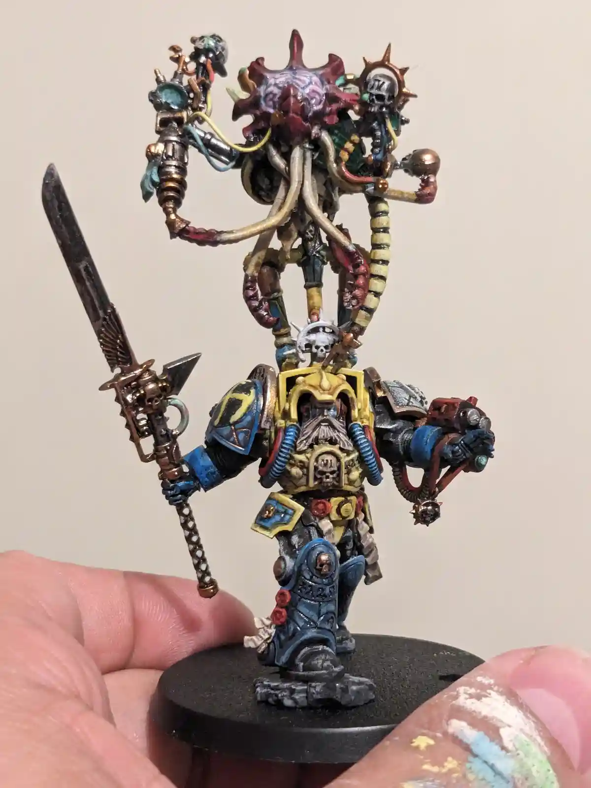 A heavily customized, painted miniature of a Warhammer 40,000 character, likely a Chaos Space Marine or similar, is held in…